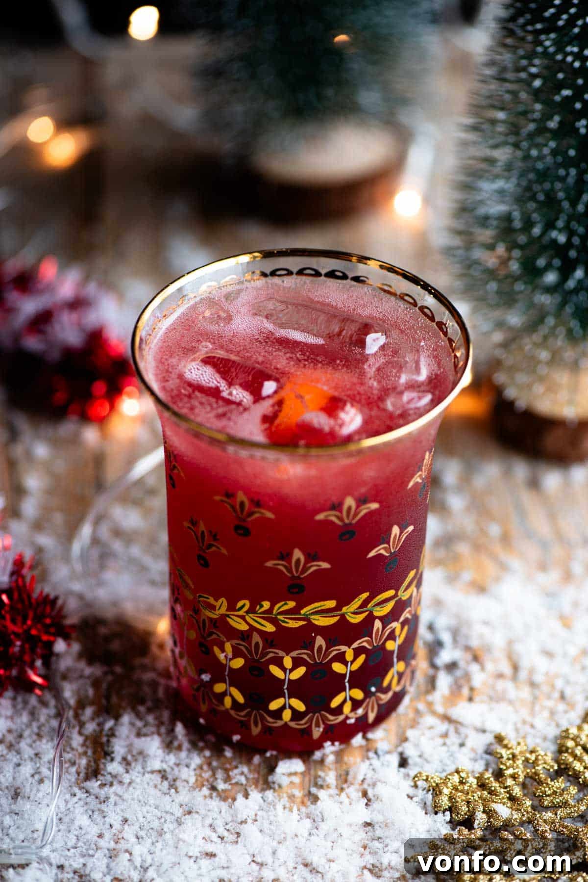 Festive Spiced Cranberry Prosecco Spritz 2 A close up of a Cranberry and Prosecco cocktail in a glass with snow and Christmas decorations all around.