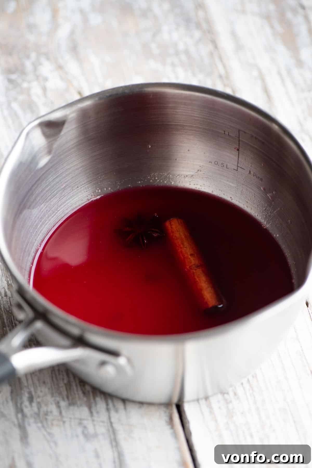 Festive Spiced Cranberry Prosecco Spritz 3 A small pot with cranberry juice and Christmas spices inside sitting on a white wooden table.