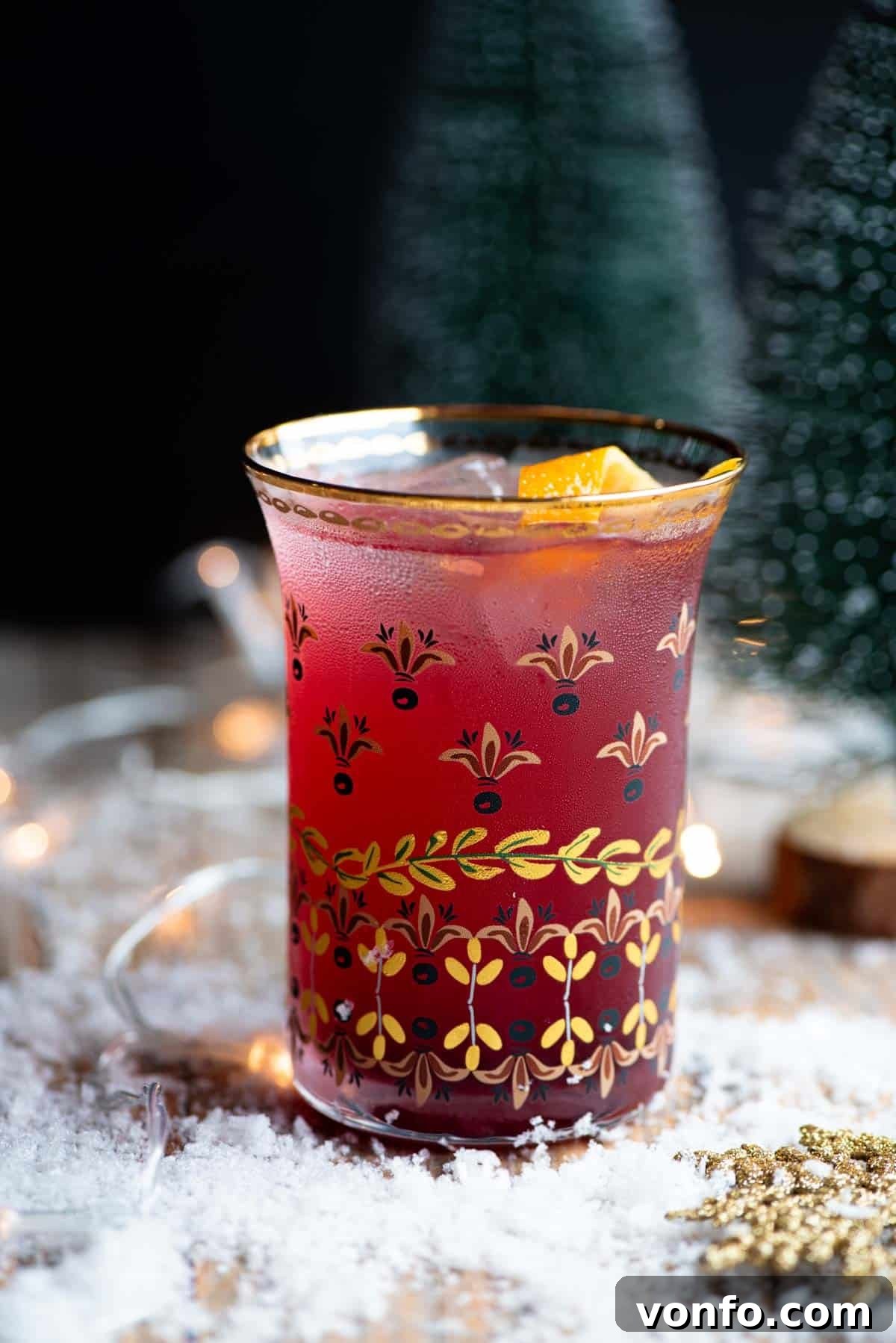 Festive Spiced Cranberry Prosecco Spritz 4 A close up side shot of a Cranberry and Prosecco cocktail sitting on a wooden table with snow all around.