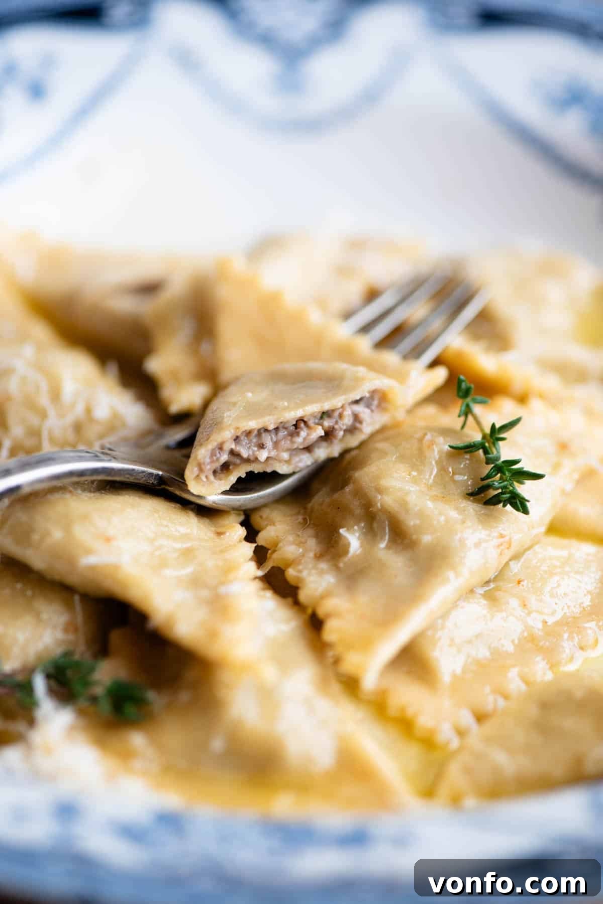 A close up side shot of cooked mushroom and taleggio Triangoli pasta in a bowl, with one pasta piece delicately cut open to reveal the rich, creamy filling inside.