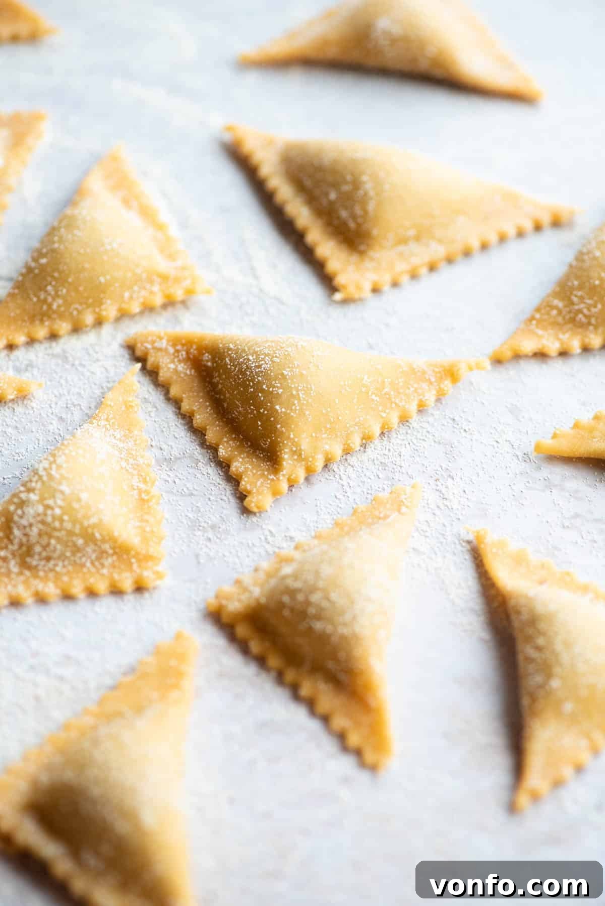 A close up side shot of neatly arranged fresh Triangoli pasta pieces on a light grey coloured board, showcasing their perfect triangular form and readiness for cooking.