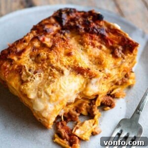 A close up of a slice of lamb lasagna on a plate with a fork at the side, showing the intricate layers.