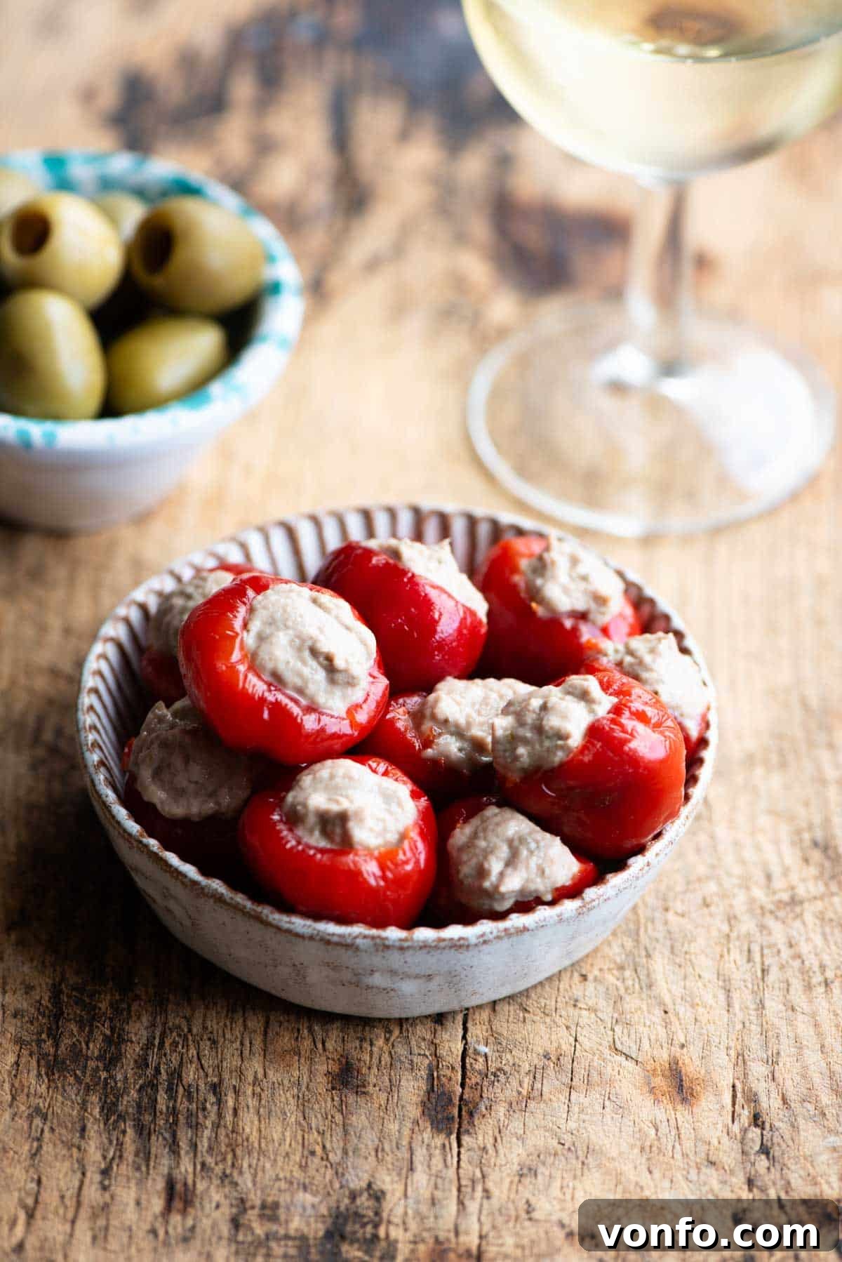 Zesty Tuna Stuffed Cherry Pepper Bites 2 Tuna stuffed cherry peppers in a small dish with olives and a glass of wine at the side.