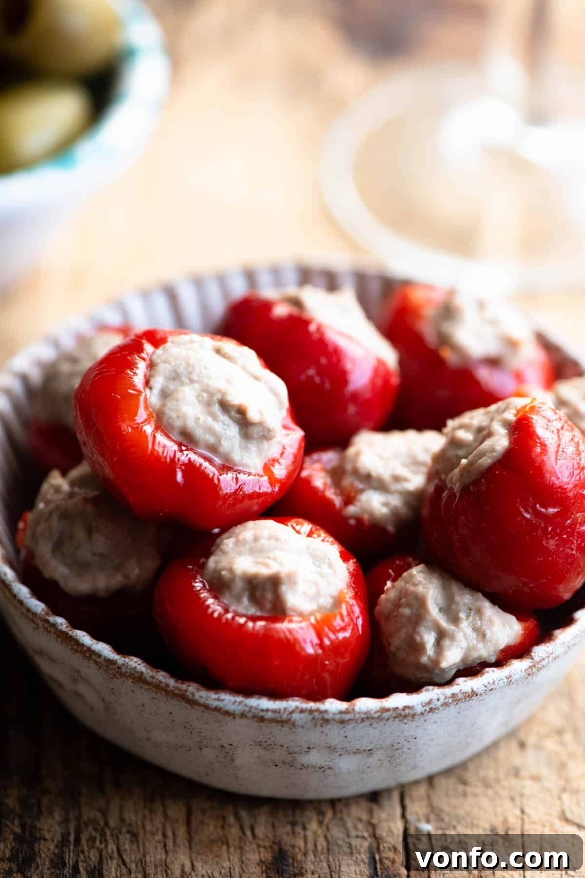 Zesty Tuna Stuffed Cherry Pepper Bites 5 A close up of tuna stuffed cherry peppers in a small dish sitting on a wooden surface.