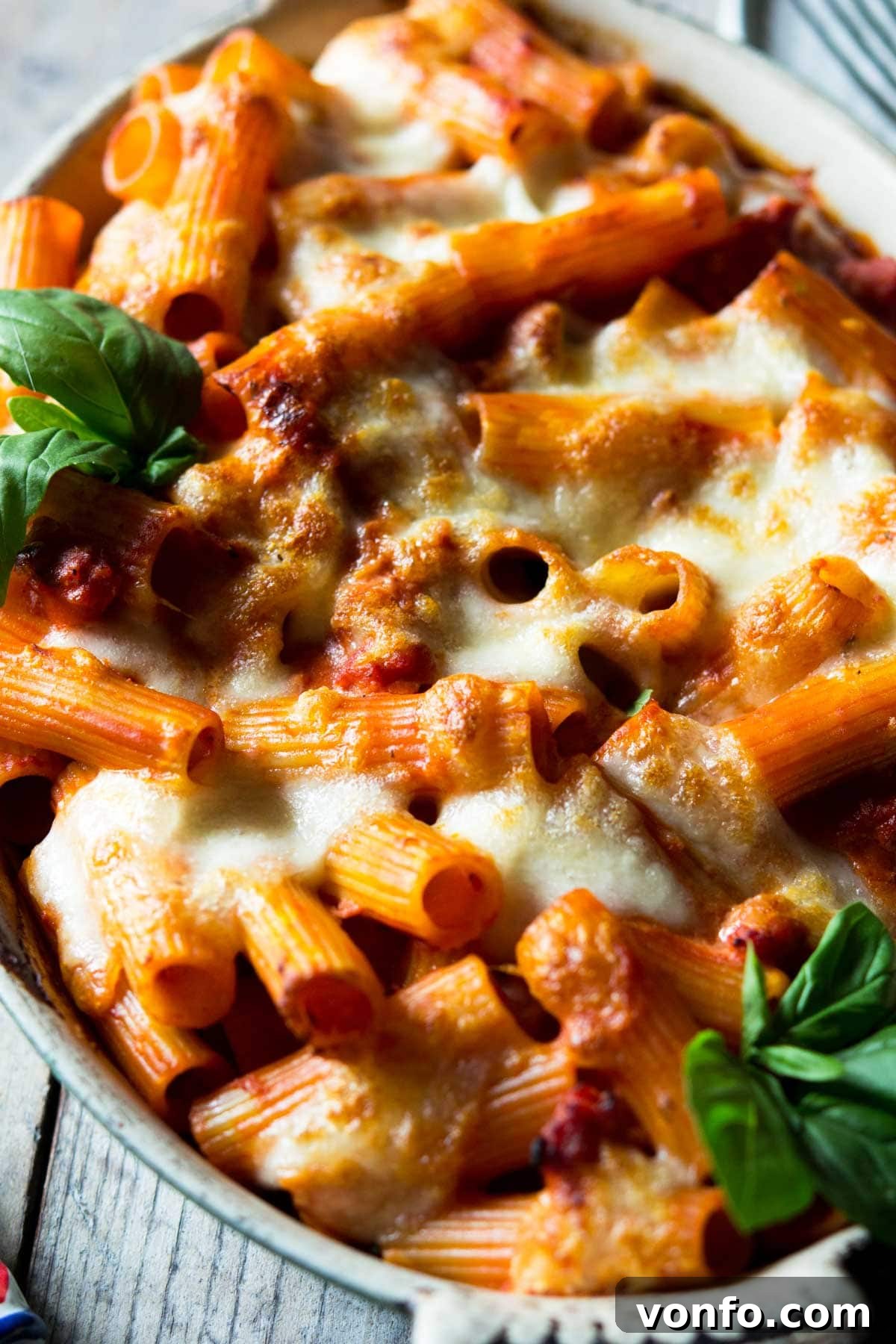 A close up of bubbling, cheesy baked pasta with sausage and tomato sauce.