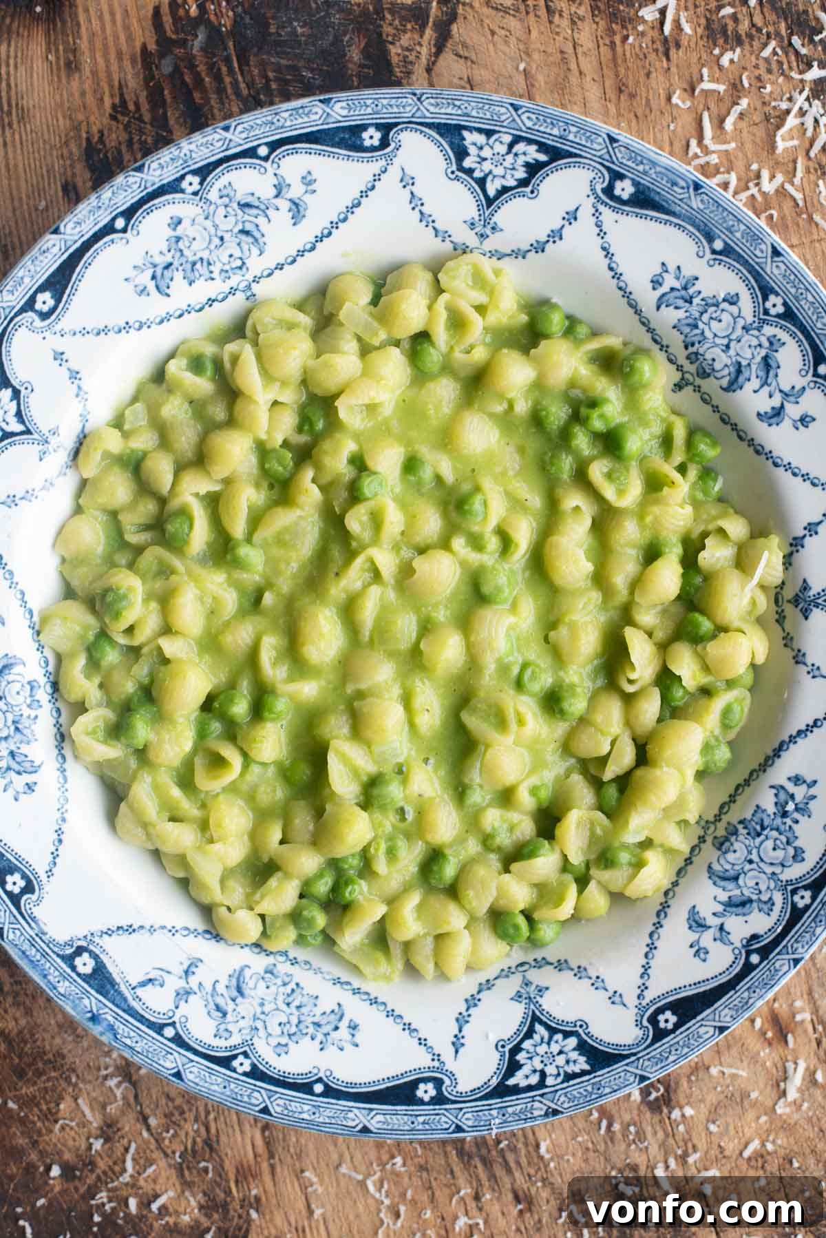 An overhead shot of a vibrant blue bowl filled with creamy Pasta e Piselli (pasta and peas), resting invitingly on a rustic wooden surface.