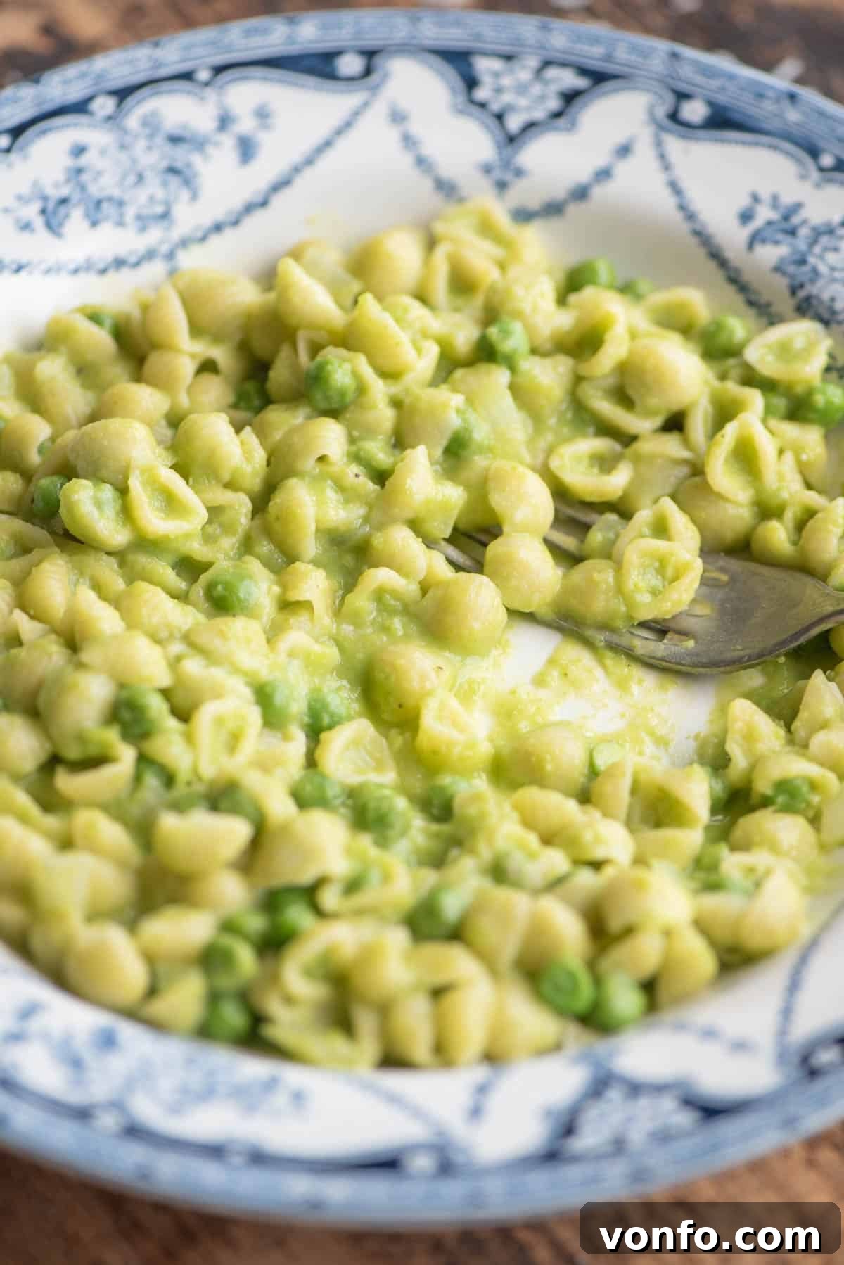 A beautiful side shot of creamy pasta and peas served in a blue patterned bowl, with a fork resting invitingly.