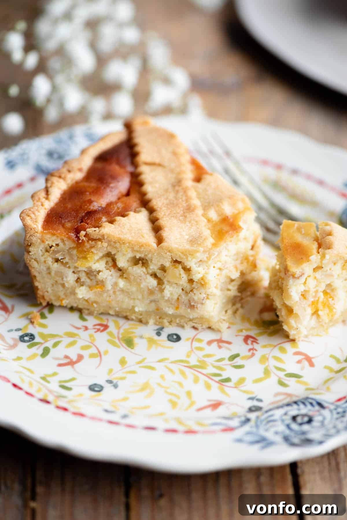 Naples' Beloved Wheat Berry Pie 11 A slice of Pastiera Napoletana on a patterned plate with white flowers in the background.