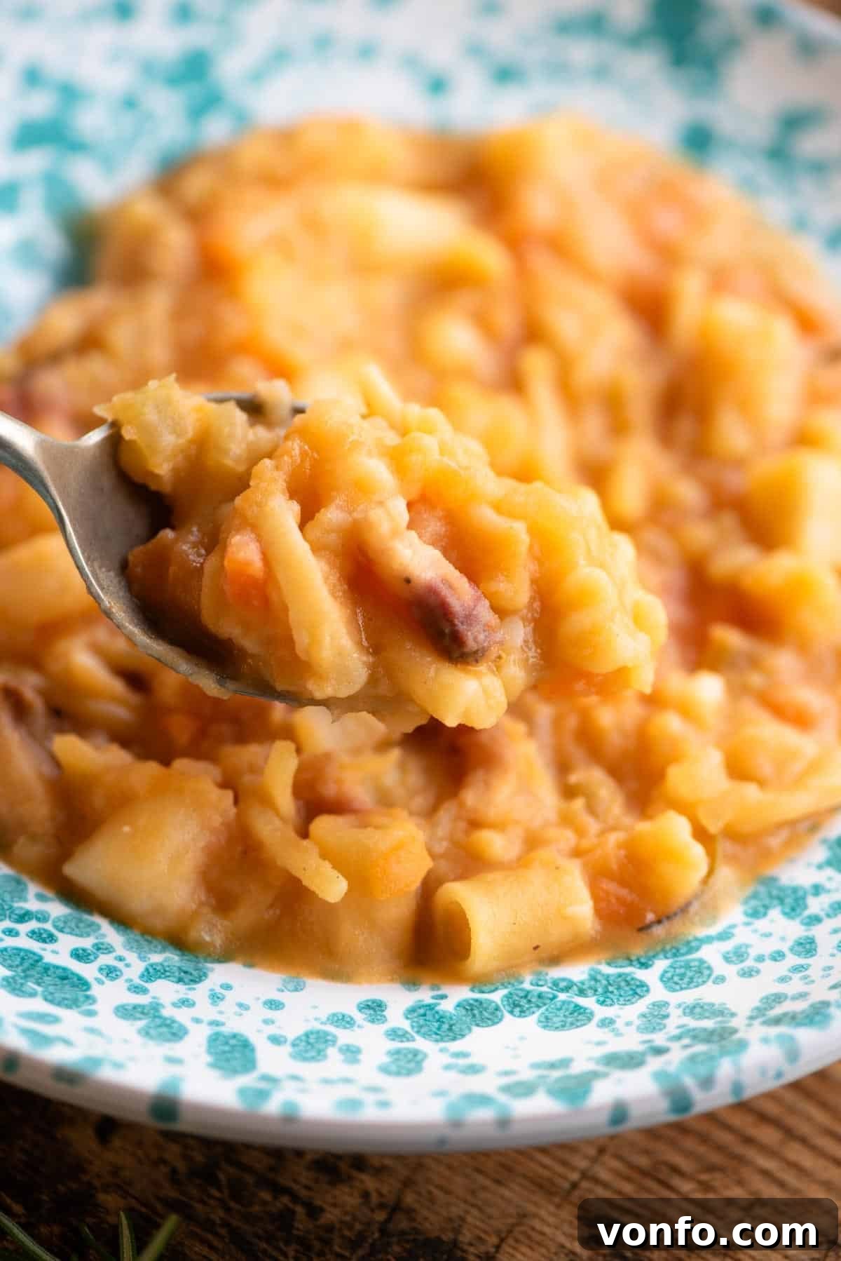 A close-up of a spoonful of creamy Pasta e Patate, held over a bowl, highlighting the tender potatoes and mixed pasta shapes.