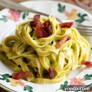 A cropped square image of pistachio pasta on a floral patterned plate topped with crispy guanciale (bacon), showcasing the rich texture and appealing presentation.