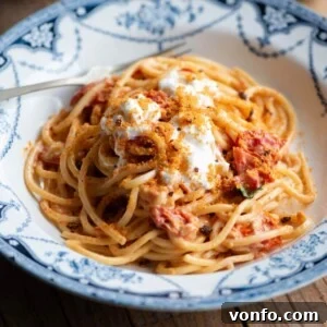 A cropped image of spaghetti in a roasted cherry tomato sauce in a blue bowl, garnished.