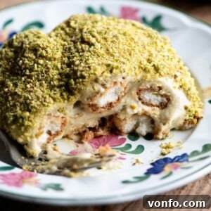 A close up of a slice of pistachio tiramisu on a floral plate, showing the beautiful layers and crumb topping.