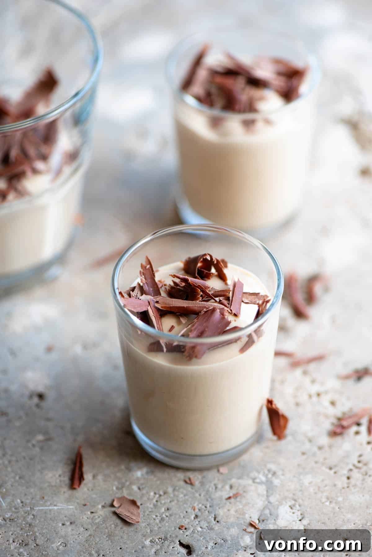 Coffee Ricotta 2 Two small glass cups filled with Ricotta al Caffè, a creamy coffee-flavored ricotta dessert, topped with dark chocolate shavings. The background features a rustic stone surface.
