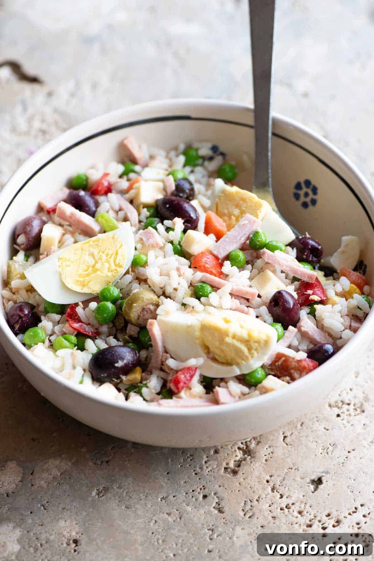 Refreshing Italian Rice Salad 2 A traditional Italian rice salad in a rustic bowl, showcasing a medley of colorful ingredients like rice, tuna, ham, and various pickled vegetables, set against a stone countertop.