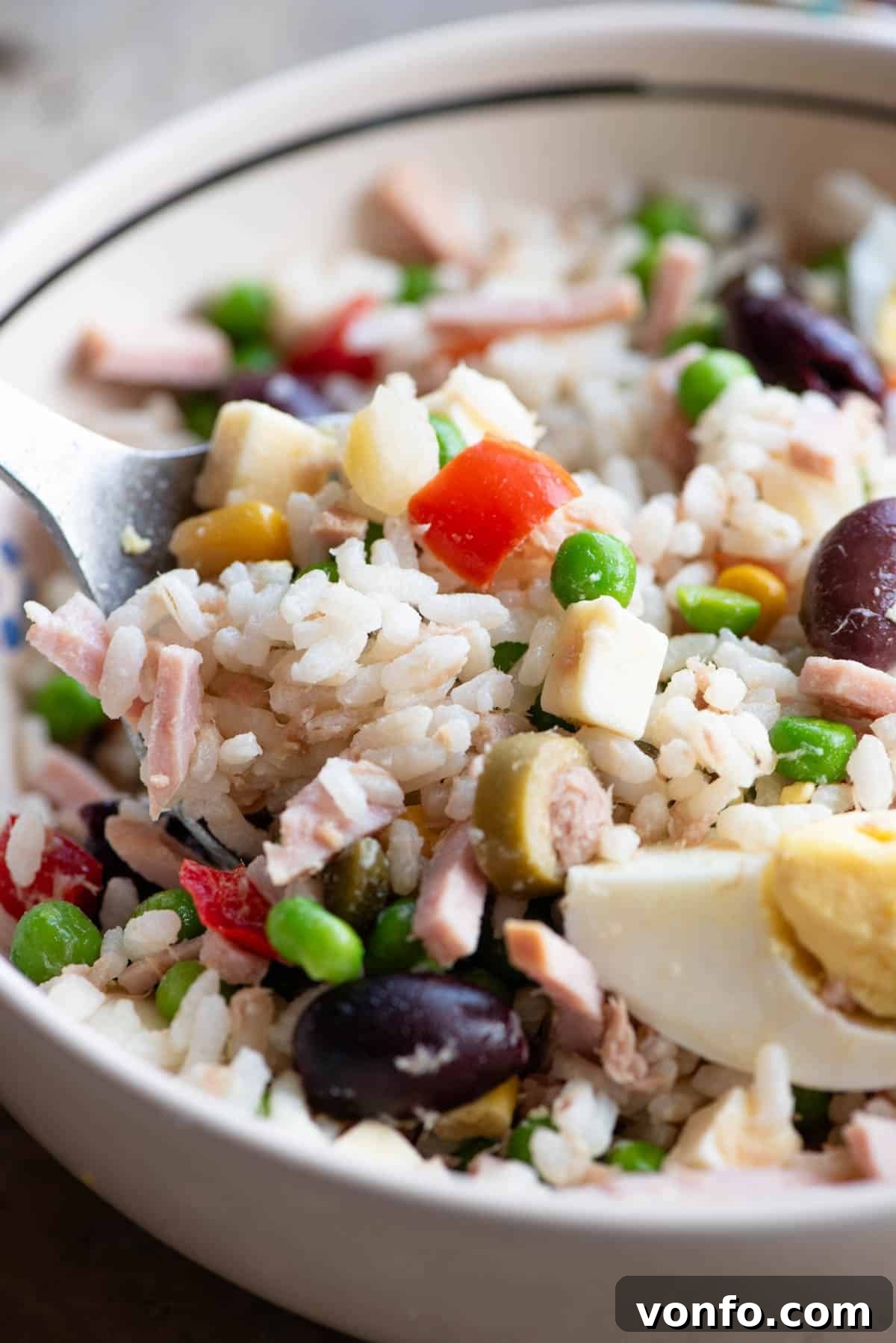 Refreshing Italian Rice Salad 5 A close-up shot of a beautifully prepared Italian rice salad in a bowl, highlighting the rich textures and colors of mixed vegetables, savory ham, succulent tuna, and perfectly hard-boiled eggs.