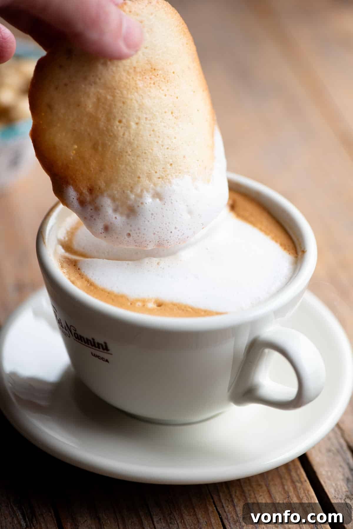 A close-up shot of a Tegola Valdostana cookie being perfectly dunked into a frothy cappuccino, highlighting its crispy texture.