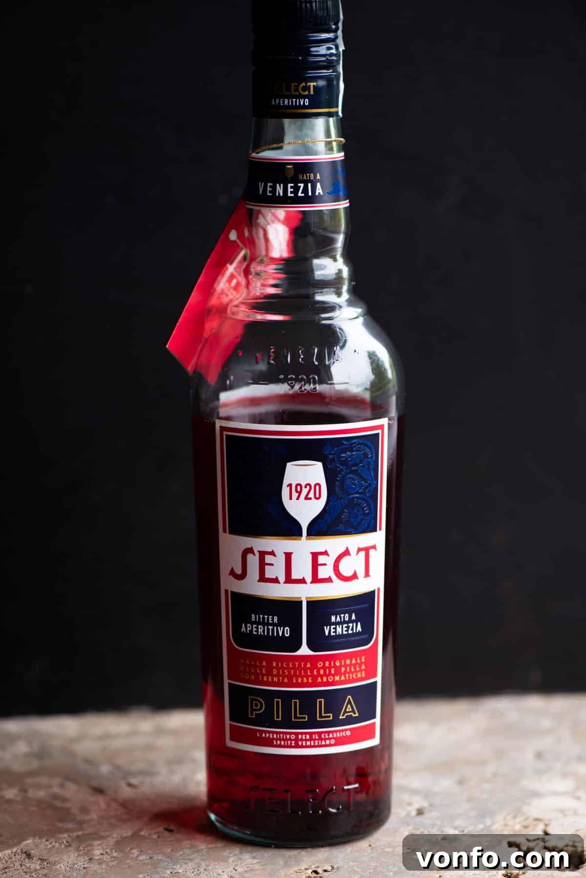Select's Venetian Sunrise 3 A bottle of Select Aperitivo standing on a rustic stone work surface against a dark background, highlighting its distinctive label.