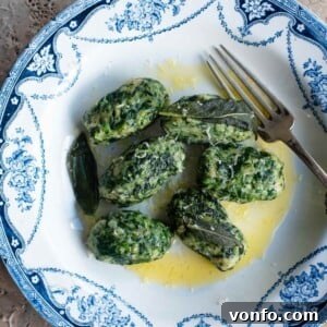 An overhead cropped image of Italian spinach and bread dumplings in a blue and white bowl with a butter sauce.
