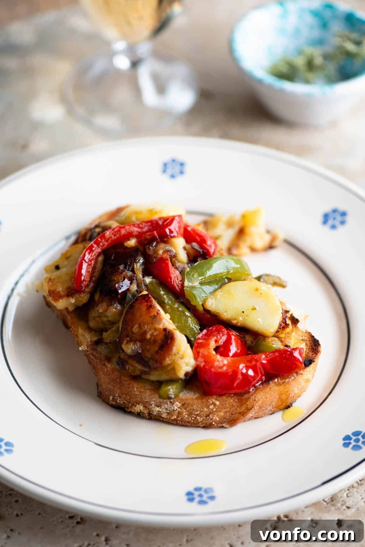 A side shot of Pipi e Patati, peppers and potatoes, served on a slice of crusty bread sitting on a plate, ready to be enjoyed.
