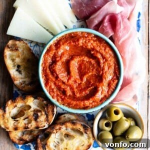 A cropped image of Ajvar, a red pepper dip in a blue bowl surrounded by antipasti, highlighting its vibrant color.