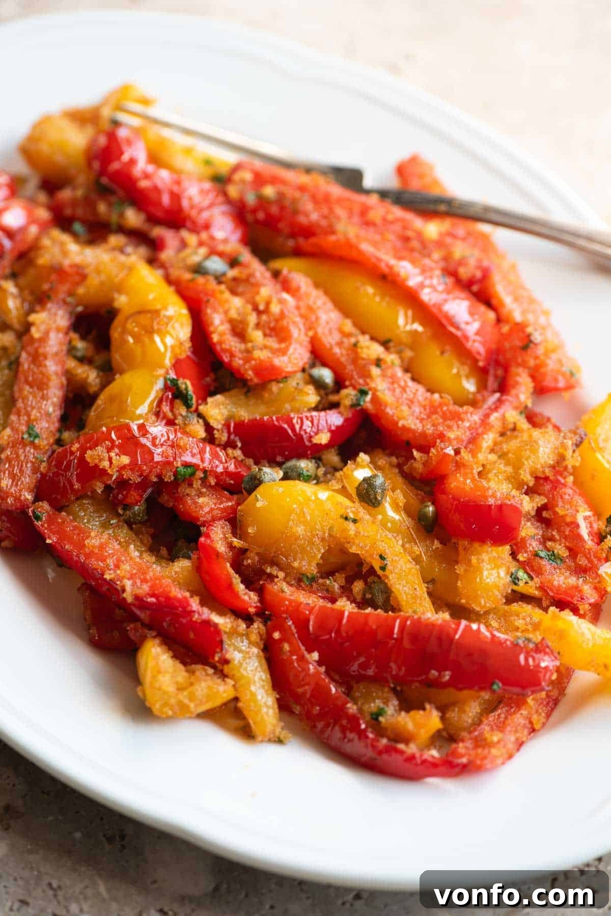 Rustic Peppers and Crispy Breadcrumbs 6 A close up side shot of mixed red and yellow peppers on a white servings dish with capers and breadcrumbs, highlighting the dish's texture and vibrant colors.