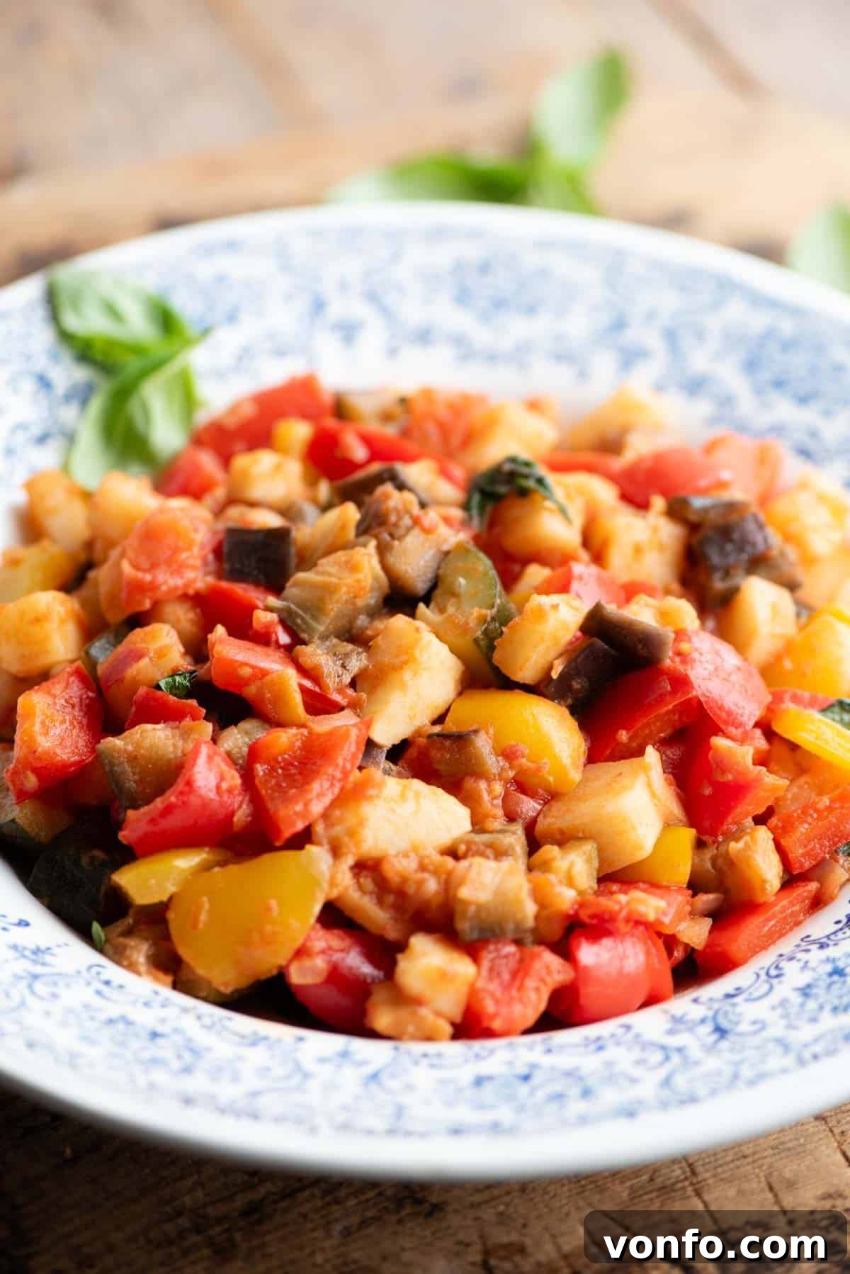 A side shot of Ciambotta vegetable stew in a blue and white bowl sitting on a wooden board.