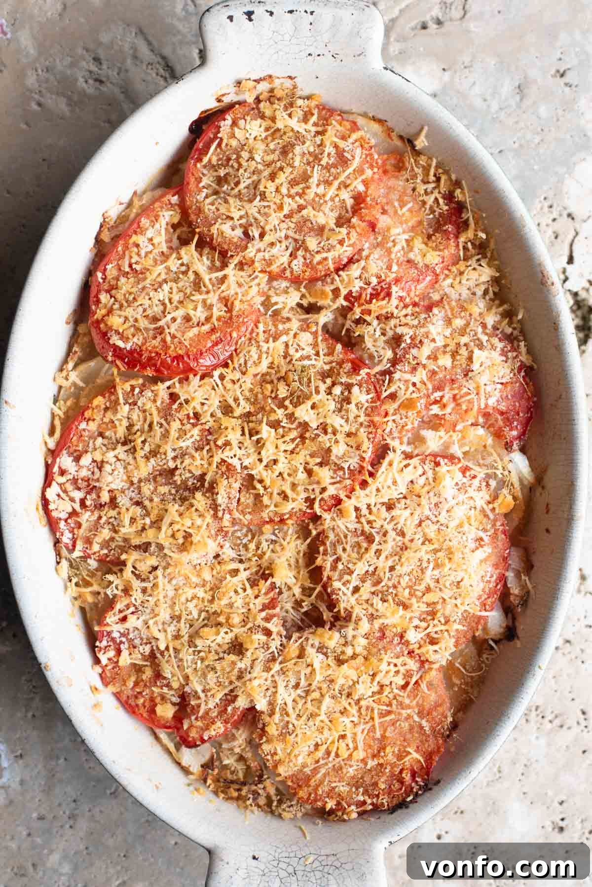 Southern Italian Potato Gratin 2 An overhead shot of a rustic Italian potato and tomato gratin, Patate alla Lucana, in an oval baking dish, resting on a textured Travertine background, highlighting its golden-brown breadcrumb crust.
