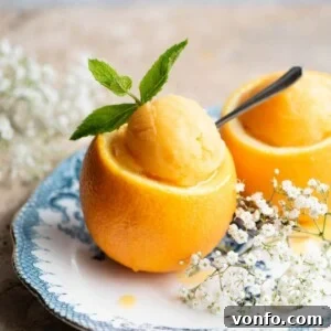 A close up cropped image of orange sorbet in a whole orange topped with a sprig of mint, ready to be served.
