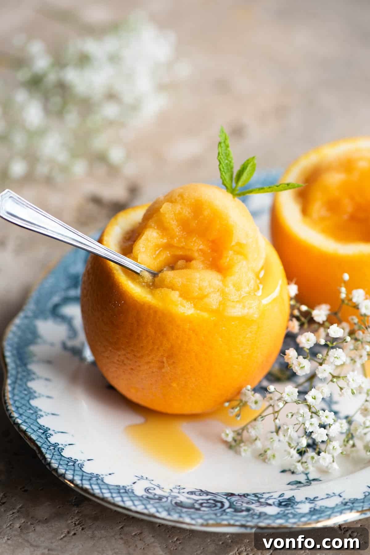 Effortless Orange Sorbet 6 A close-up shot of orange sorbet beautifully served inside an orange half, resting on a blue plate with decorative flowers in the background.