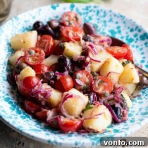 A close up cropped image of a Sicilian potato salad in a blue bowl with olives, onions, and tomatoes.