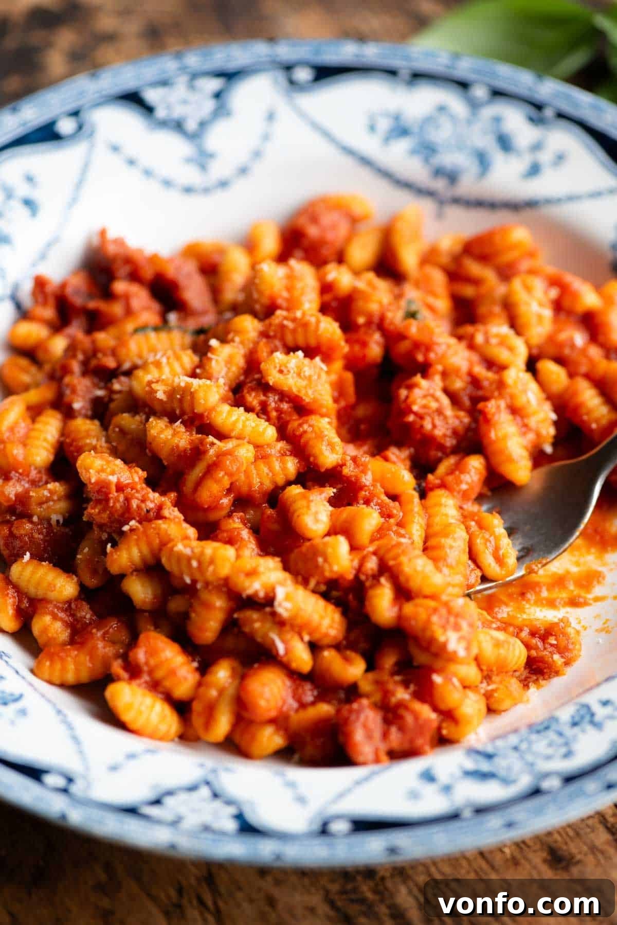 A close up side shot of a Sardinian sausage pasta in a blue and white bowl with a fork, showing the texture and rich sauce of Malloreddus alla Campidanese.