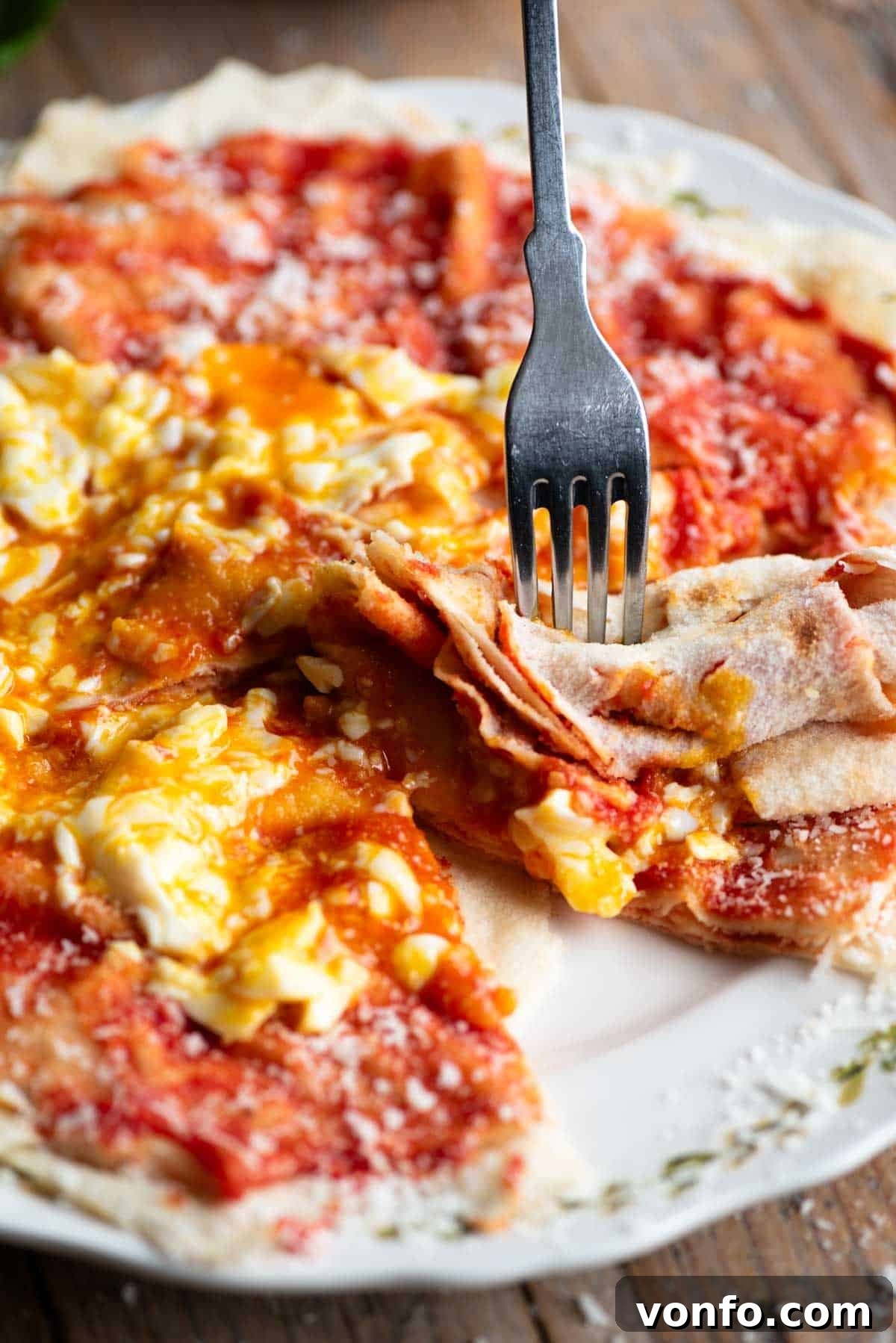 A fork gently breaking into a piece of Pane Frattau, revealing the delightful layers of bread, tomato sauce, and a luscious, runny poached egg yolk.