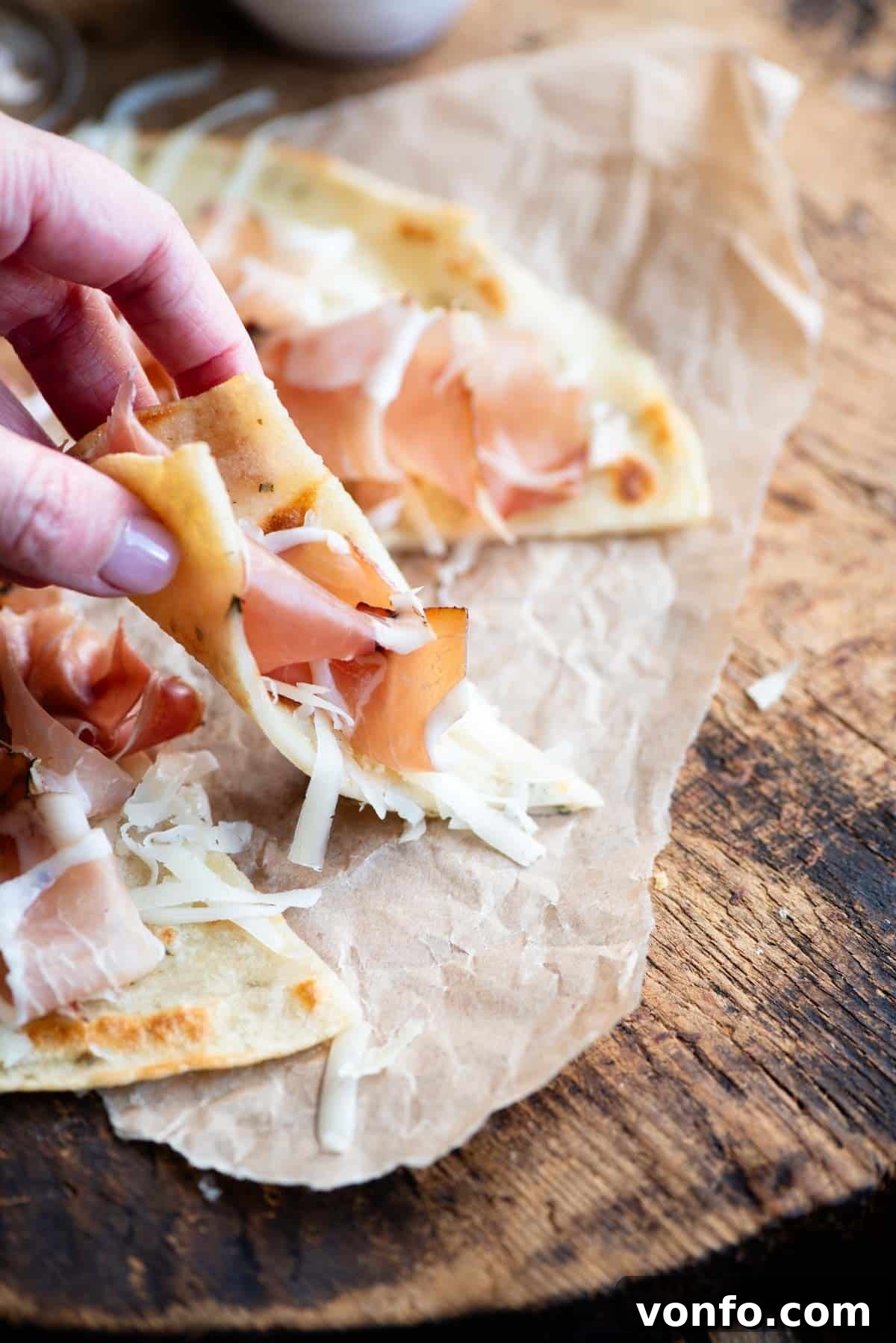 Brustengo Rustic Umbrian Flatbread 6 A hand picking up a slice of Italian flatbread topped with cured meat and cheese, showcasing the inviting texture of Brustengo.