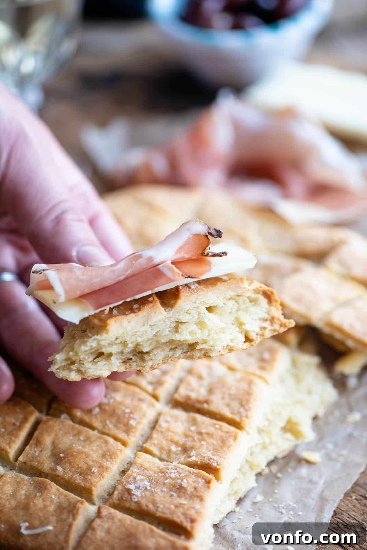Abruzzo's Rustic Hearth Flatbread 7 A close up of a hand holding a piece if Pizza Scima with cured meat.