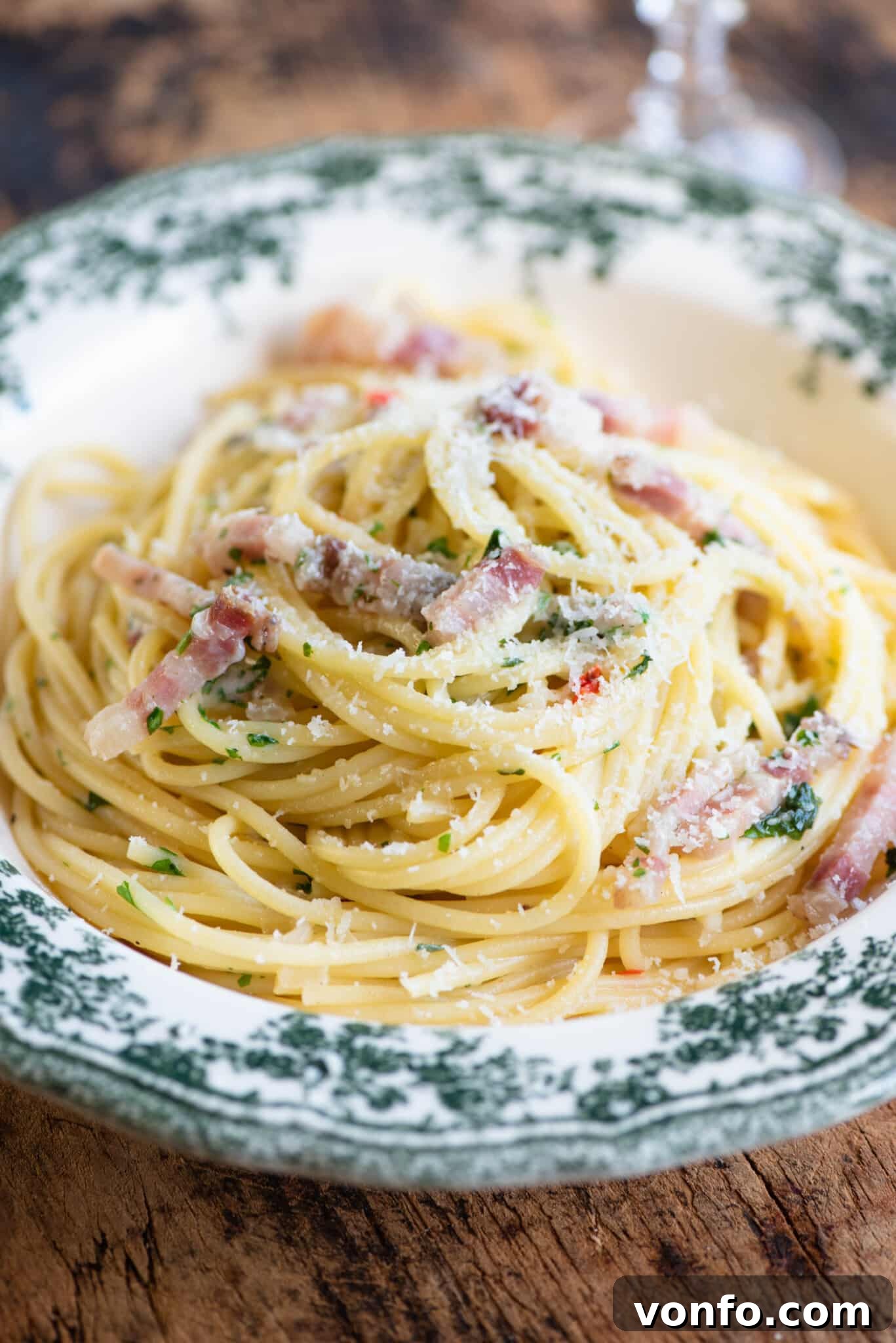 Spaghetti alla Molisana with Smoky Pancetta, Fresh Herbs, and Spicy Chili 6 A close up of spaghetti topped with pancetta and onions in a green patterned bowl.