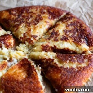 Frico Golden Cheesy Potato Onion Cake 8 A close-up shot of a golden-brown, cheesy potato cake (Frico) sliced into perfectly portioned wedges on a plate, revealing its soft, gooey interior.