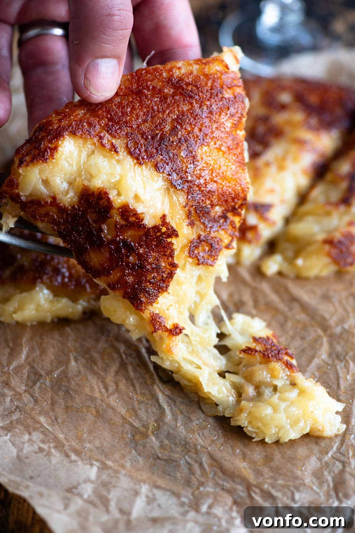 Frico Golden Cheesy Potato Onion Cake 7 A hand reaching for a slice of Frico (fried cheese and potato cake) from a rustic wooden serving board, highlighting its appealing texture and tempting golden crust.