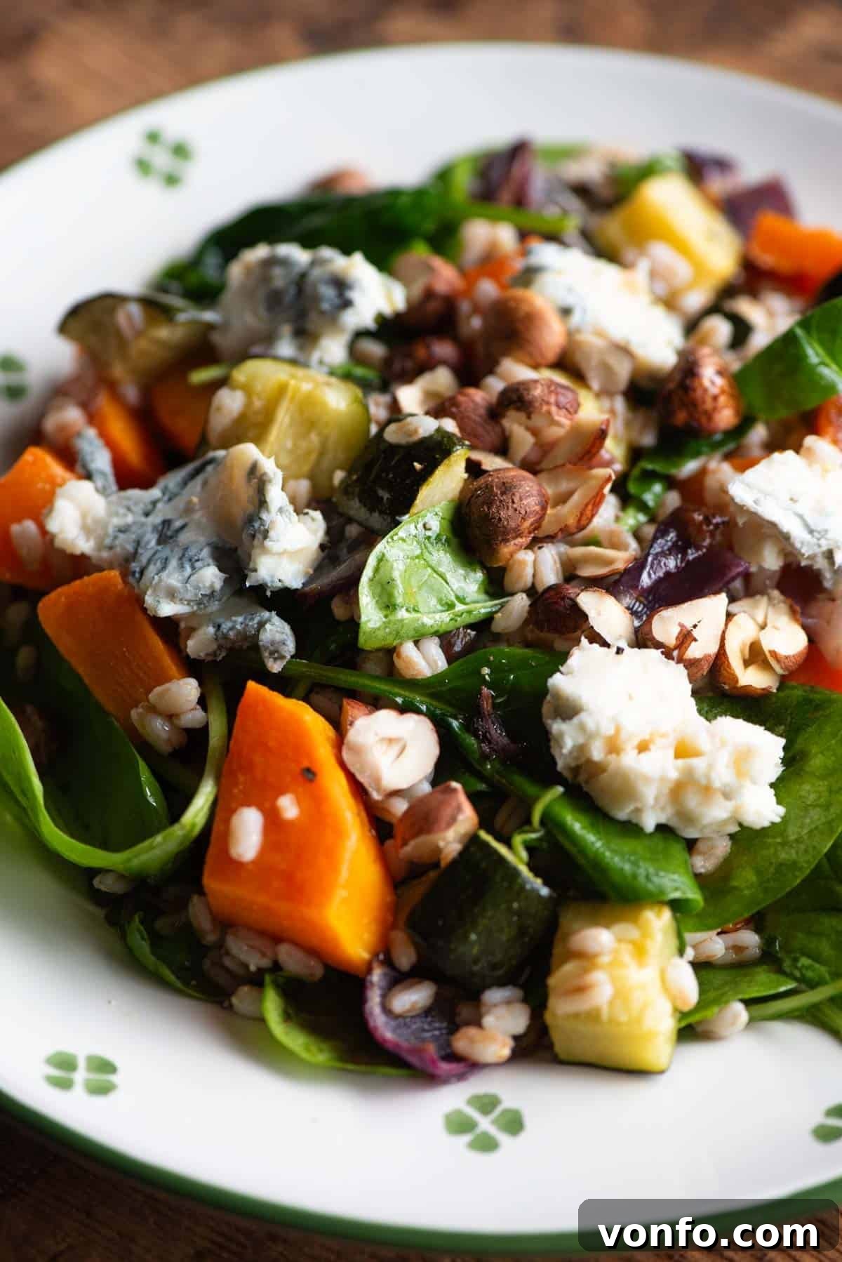 A close up of a warm farro salad on a plate with butternut squash, spinach and gorgonzola, showcasing its rich textures and vibrant colors.
