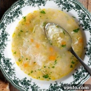 A cropped close up of rice soup in a green and white bowl with a spoon inside, ready to be enjoyed.