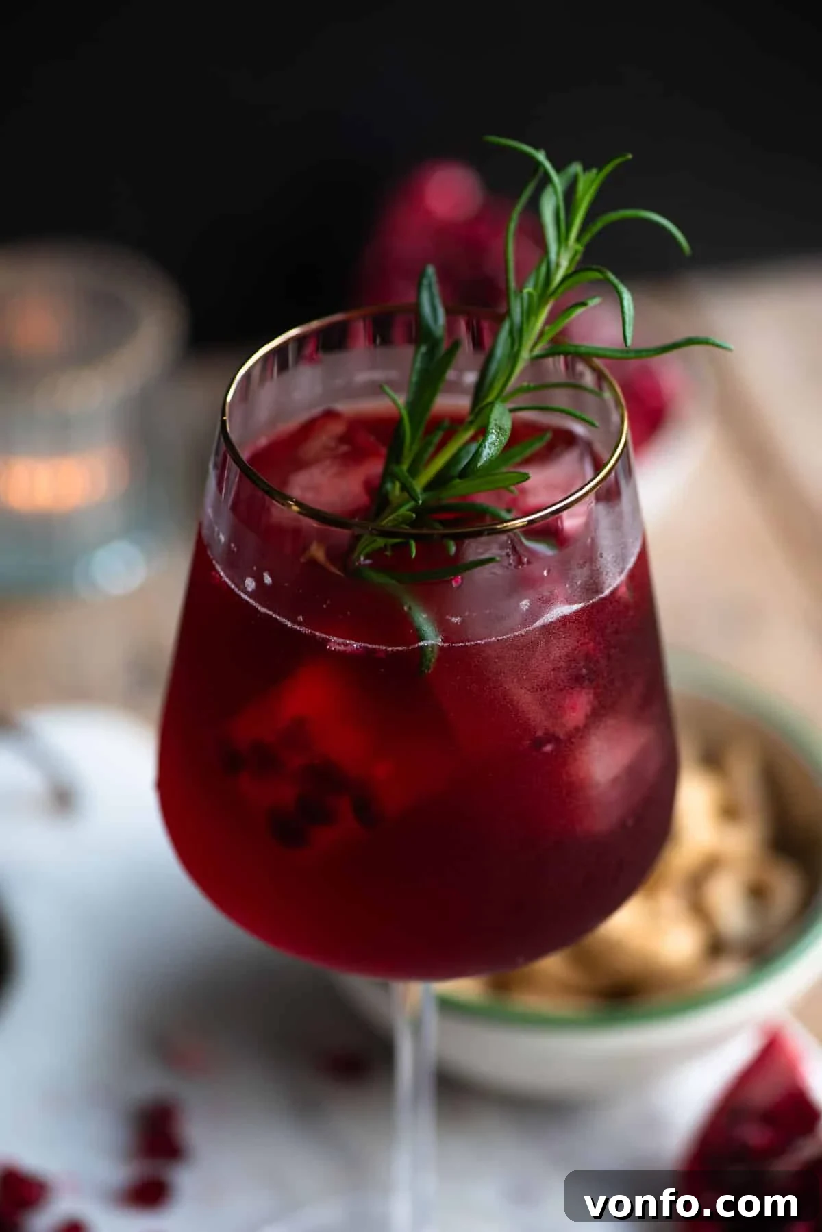 Pomegranate Spritzers 4 A beautifully crafted Pomegranate Spritz, captured in a close-up shot within a wine glass, adorned with a delicate rosemary sprig, emphasizing its vibrant color and festive appeal.