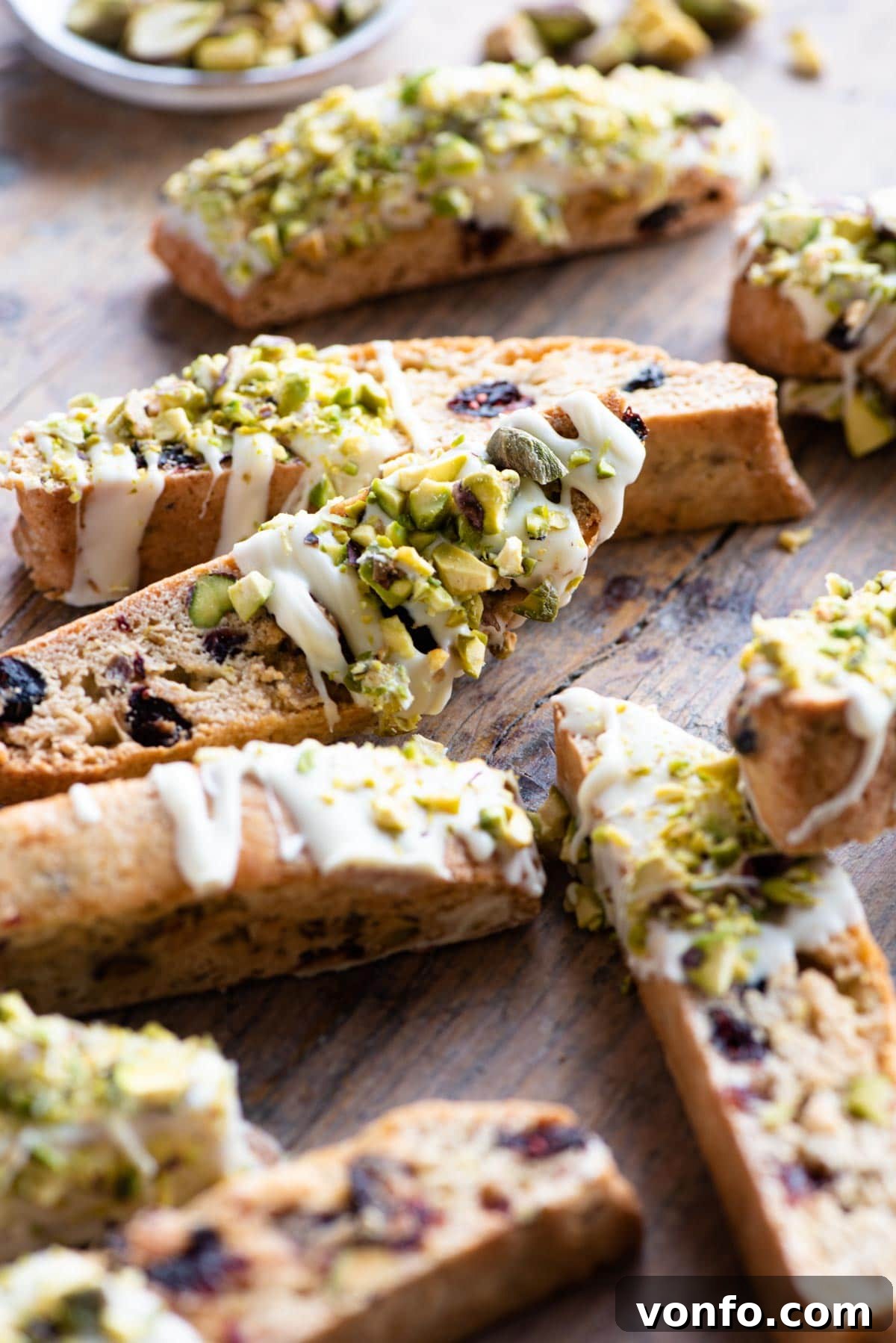 A beautiful close-up shot of Cranberry Pistachio Biscotti, artfully adorned with white chocolate drizzle, resting on a rustic wooden surface.