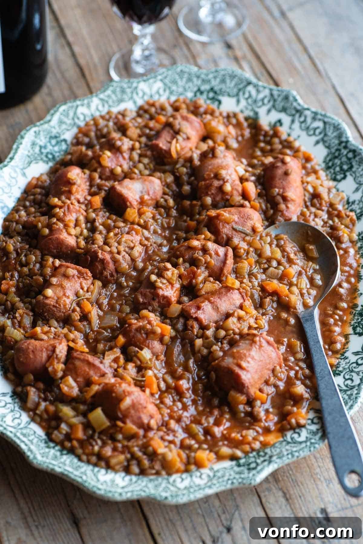 Italian sausages and lentils on a large serving plate sitting on a wooden table. A rich, warm dish ready to be enjoyed.