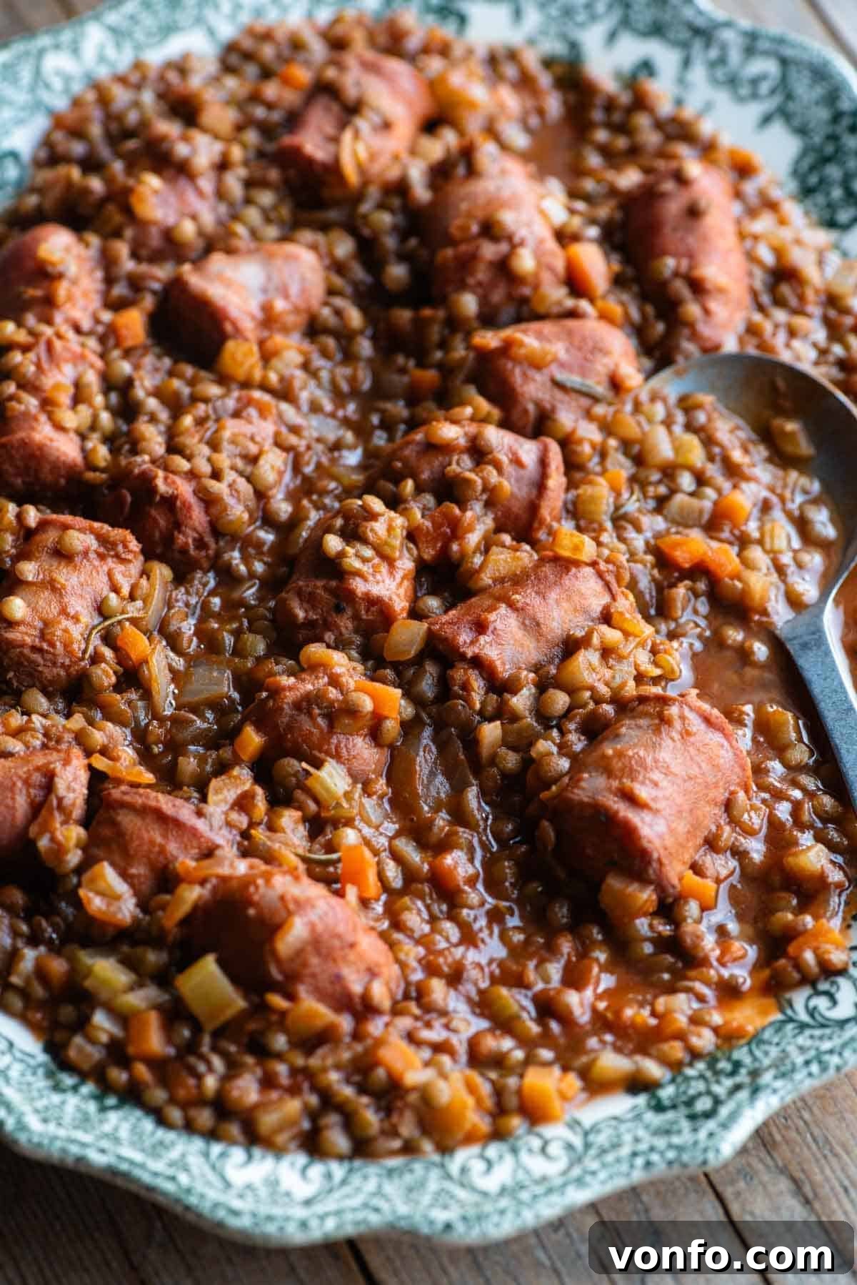 A close up of Italian sausages and lentils on a large plate with a serving spoon, highlighting the texture and richness.