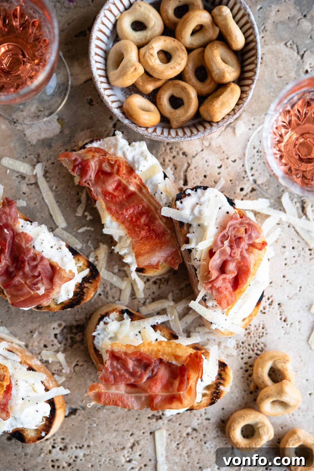 An overhead shot of burrata and Parmigiano crostini arranged on a elegant travertine background, each piece beautifully topped with crispy prosciutto, ready to be served as an appetizer.