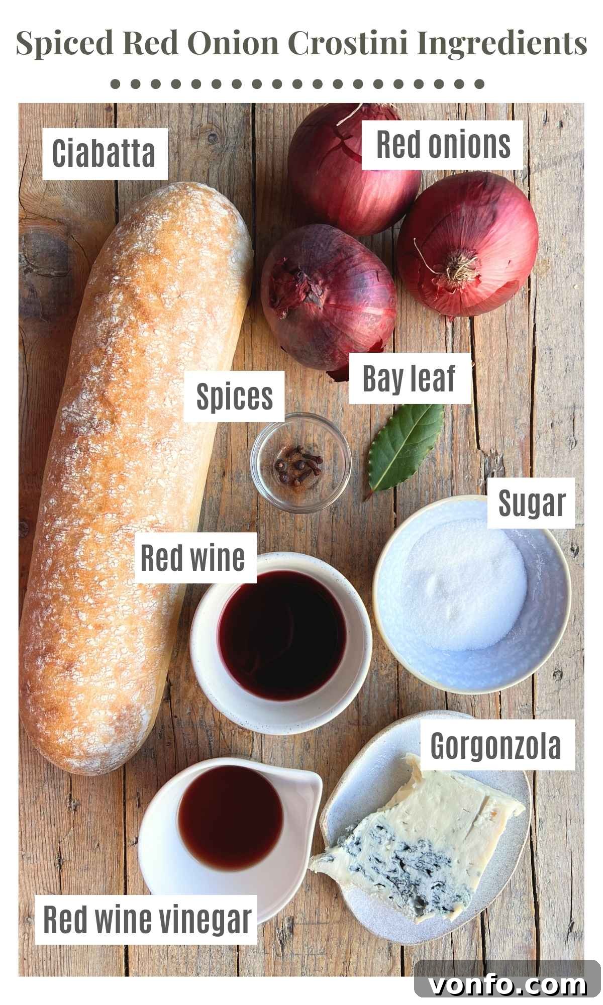 An overhead shot of all the fresh ingredients, including vibrant red onions, a selection of whole festive spices, bottles of red wine and red wine vinegar, and a block of crumbly Gorgonzola, neatly arranged for making red onion and gorgonzola crostini.