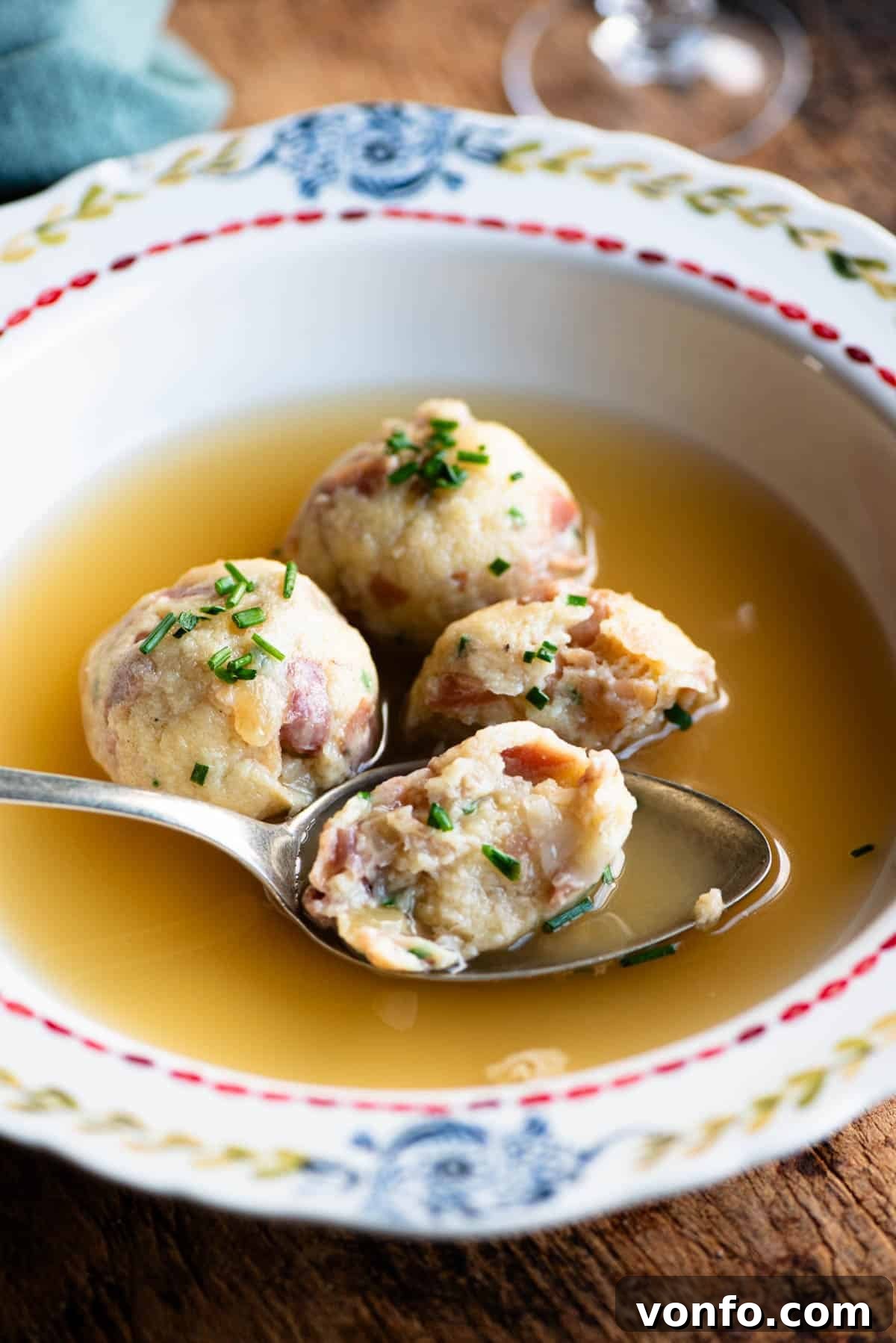 A side shot of Canederli dumplings served in a clear broth with a spoon, ready to eat.