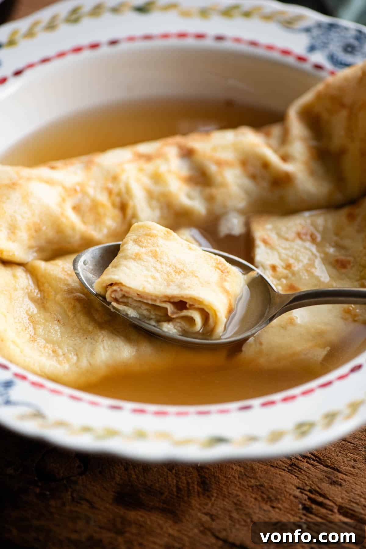 A close up of a spoon in a bowl of broth picking up a spoonful of crepe, highlighting the texture.