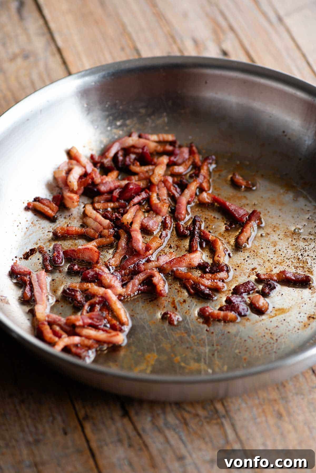 A close-up shot of a frying pan, showcasing perfectly rendered and crispy golden pancetta cubes, ready to be used as a topping.