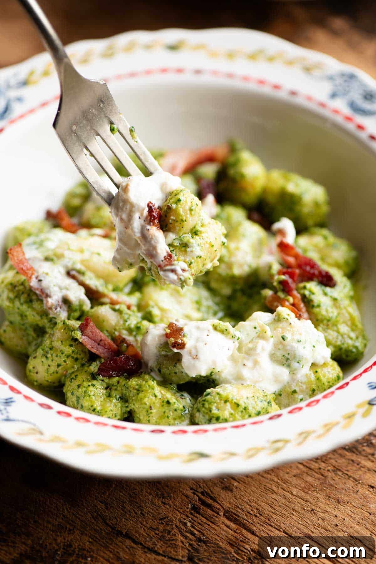 A close-up shot of a fork picking up a piece of arugula pesto gnocchi, clearly showing the rich sauce, tender gnocchi, and a hint of creamy burrata.