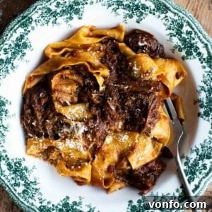 A close up of beef rib ragu with pappardelle pasta in a green and white bowl, ready to be served.